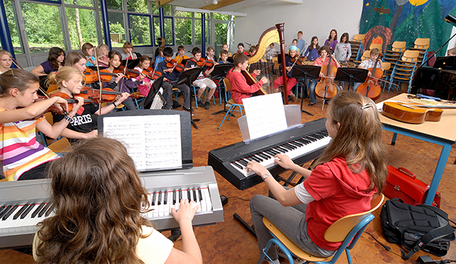 eine Gruppe Schüler mit verschiedenen Instrumenten, die in einem großen Raum sitzen und gemeinsam Musik machen