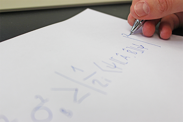 eine Hand, die eine physikalisch-mathematische Formel auf ein Papier schreibt.
