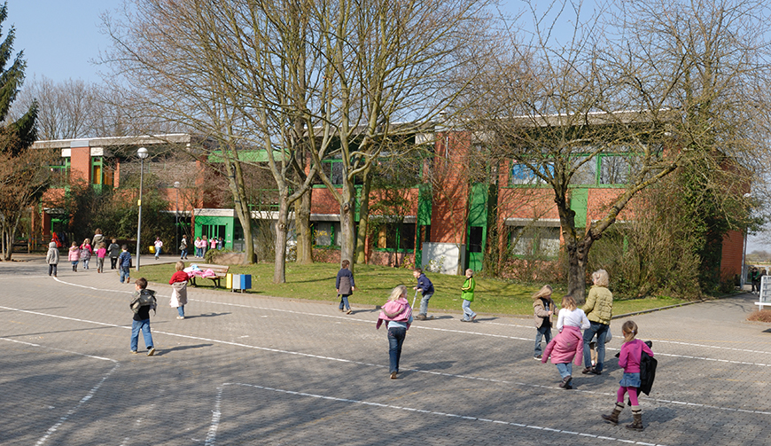 im Vordergrund ein Hof, auf dessen Boden mit weiß Straßen eingezeichnet sind und auf dem Kinder spielen; im Hintergrund Bäume und Gebäude