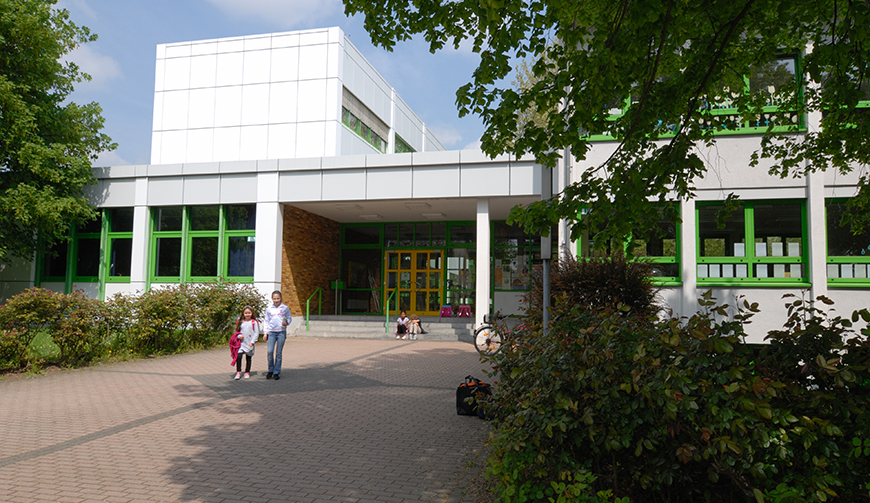 einen großen Hof und an den Bildrändern einige Hecken und Bäume; im Hintergrund ein großes Gebäude