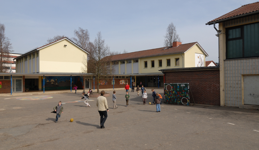 einen großen Hof, in dem einige Kinder spielen; im Hintergrund gelb gestrichene Gebäude
