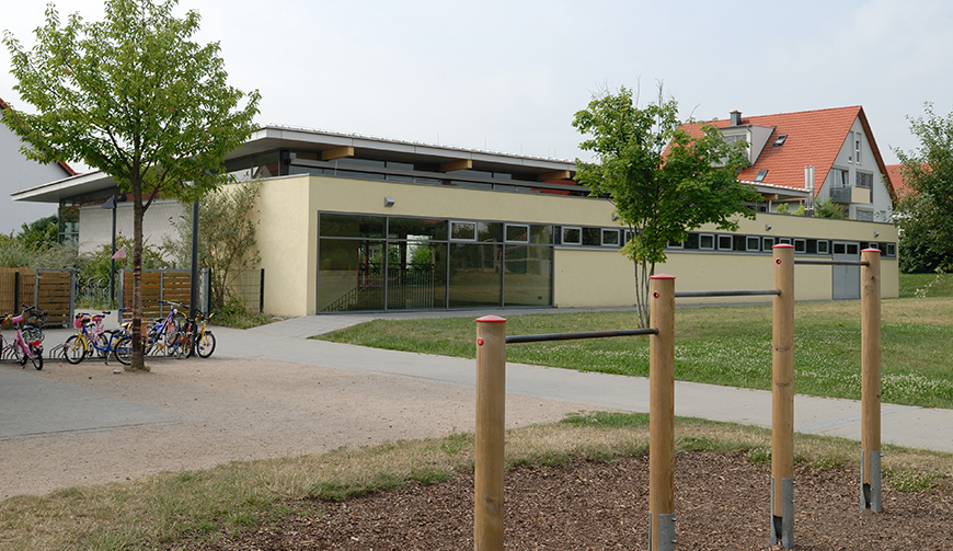 den Blick über einen kleinen Garten und einen Hof auf ein hell gestrichenes, flaches Gebäude