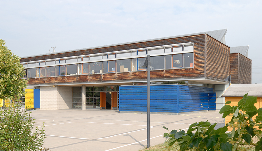 Blick über einen Hof auf ein großes, in braune und blauen Farben gehaltenes Gebäude