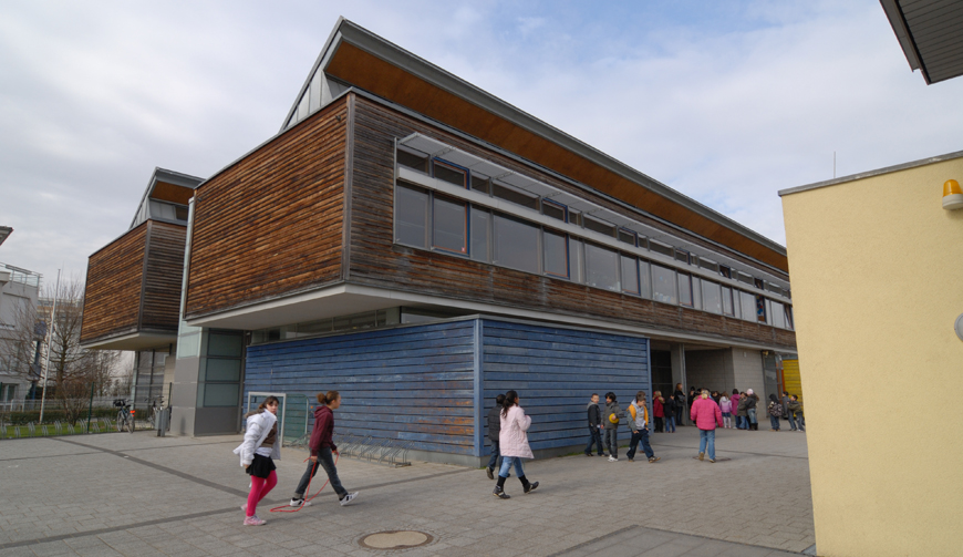 den Blick auf ein großes Gebäude, davor einige Kinder auf einem Hof