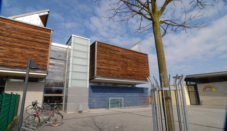 den Blick vorbei an einem Baum auf ein großes Gebäude, vor dem einige Fahrräder stehen