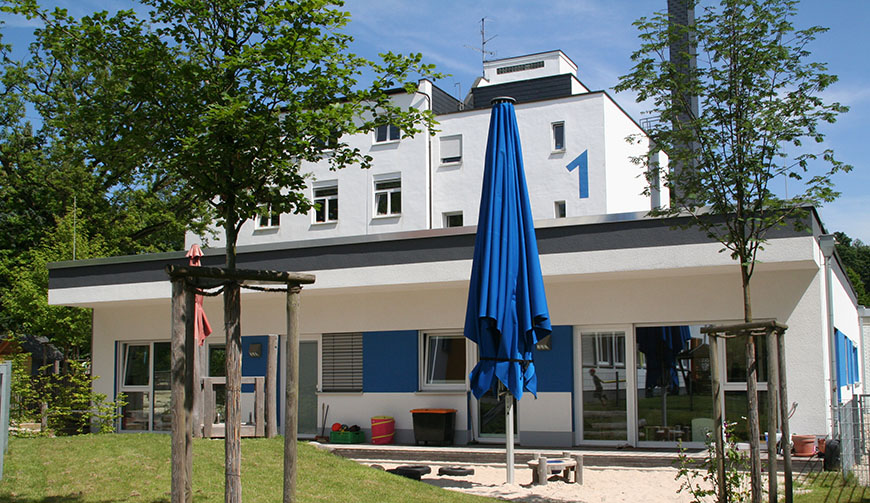 Blick auf ein weißes Gebäude, vor dem ein blauer Sonnenschirm steht