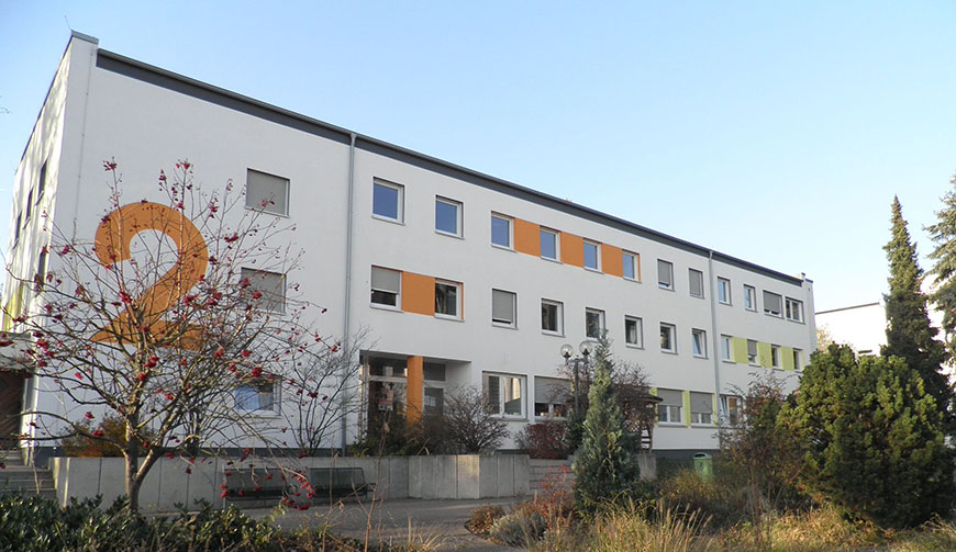 Blick auf ein großes, weißes Gebäude, auf dem mit orangener Farbe die Zahl 2 steht