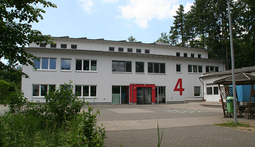 Blick über einen Hof auf ein großes weißes Gebäude, an dem mit roter Farbe die Zahl 4 steht