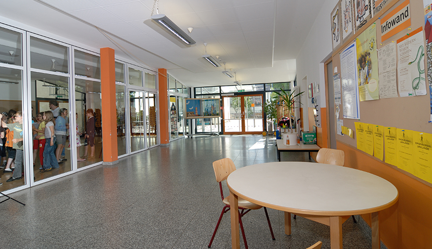 einen großen Raum mit vielen Fenstern, im Vordergrund steht ein runder Tisch mit einigen Stühlen
