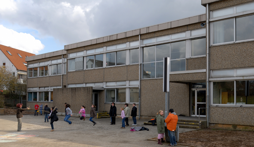 Blick auf den Ausschnitt eines Schulhofs vor einem großen Gebäude, in dem Kinder spielen
