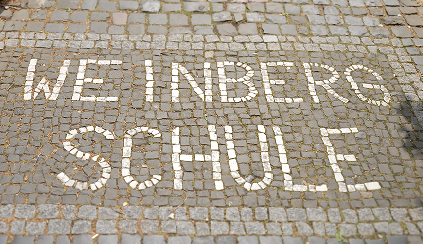 ein Stück Kopfsteinpflaster, in das mit weißen Steinen der Text Weinbergschule eingelassen ist
