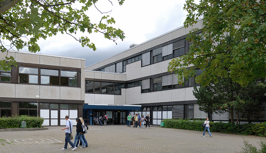 einen Hof, über den einige Schüler laufen, und im Hintergrund ein großes Gebäude