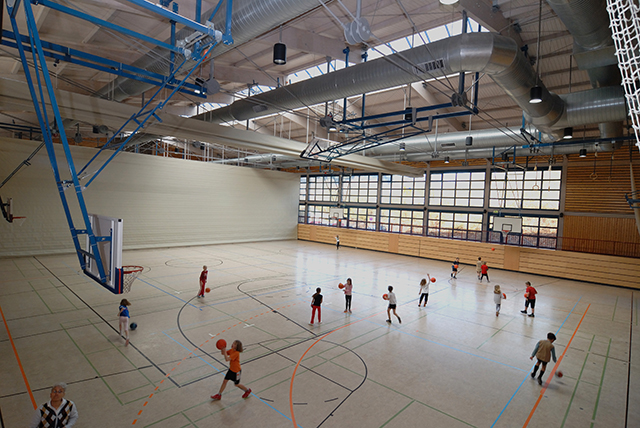 den Blick von  oben in eine Sporthalle, in der Kinder Ball spielen