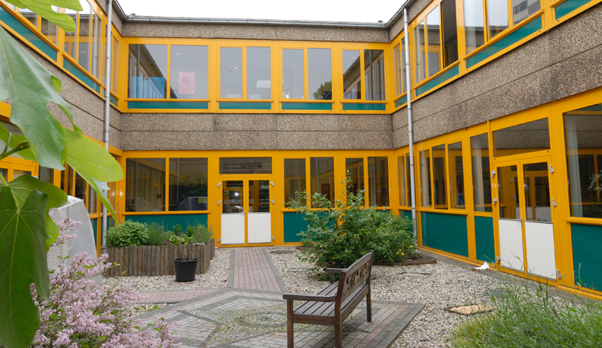 Blick in den Innenhof eines Gebäudes mit gelben Fensterrahmen, in dem eine Bank steht