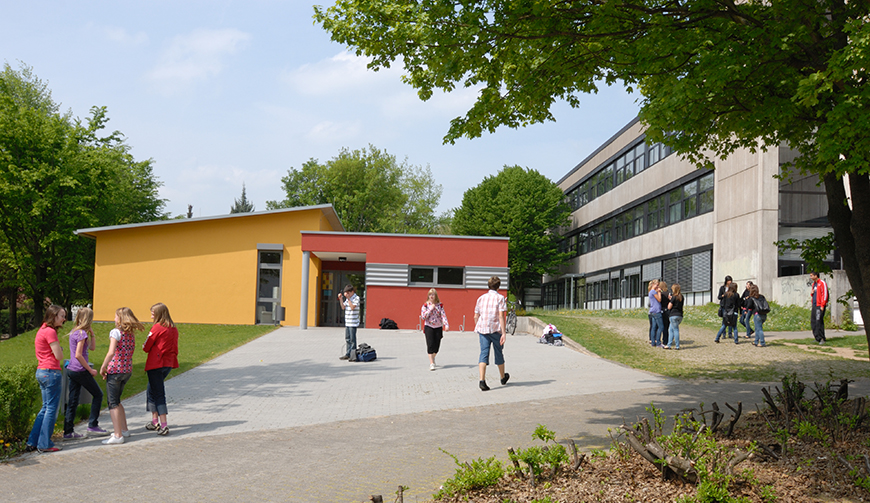 einige Schüler in einem Hof, im Hintergrund ein kleines, gelb und rot gestrichenes Gebäude
