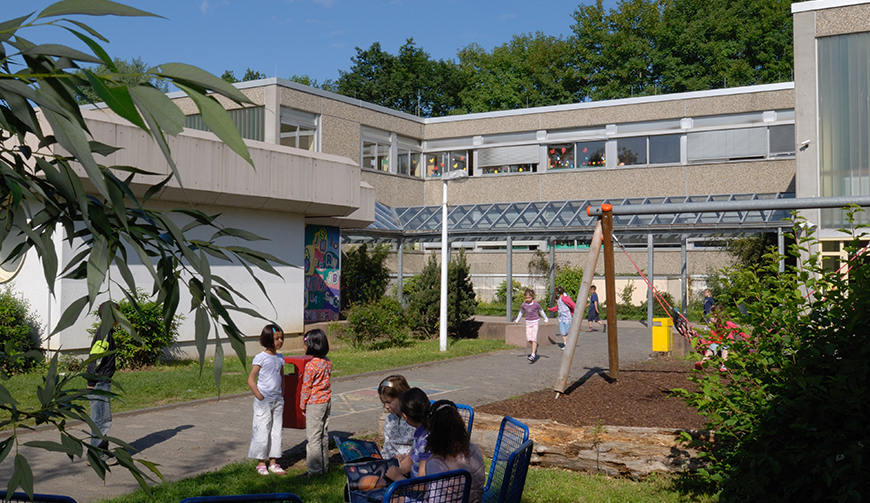 Blick über einen Schulhof mit Schaukel auf ein Gebäude