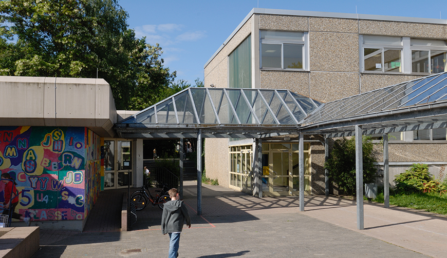 Blick in einen teilweise überdachten Innenhof mit einem Gebäude im Hintergrund und einer bunte bemalten Wand links im Bild