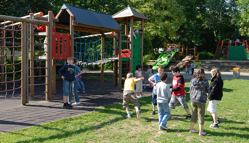 spielende Kinder auf einer Wiese mit einem Klettergerüst im Hintergrund