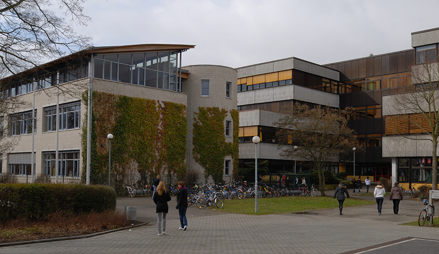 im Vordergrund einige Schüler, die über einen Hof auf ein mehrstöckiges Gebäude zugehen