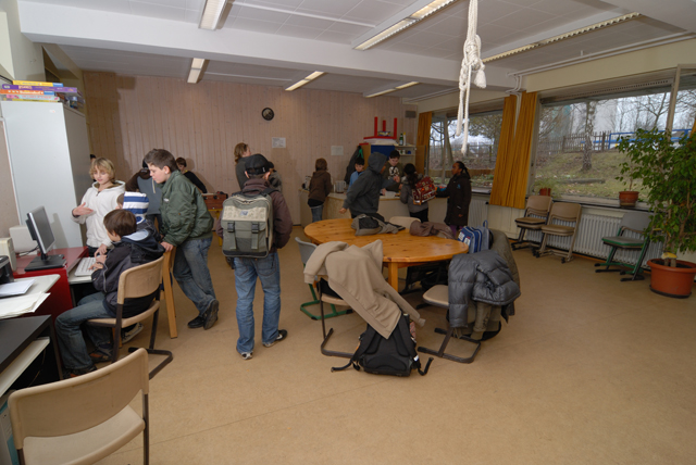 eine Gruppe Schüler in einem Computer-Arbeitsraum; im Vordergrund ein Tisch und Stühle, über denen Jacken hängen
