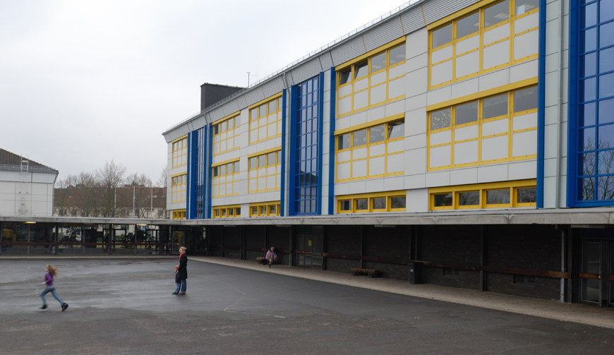 Blick über einen Schulhof auf ein gelb-blaues Gebäude