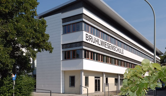 den Blick auf ein langgestrecktes weißes Gebäude mit dem Schriftzug Brühlwiesenschule