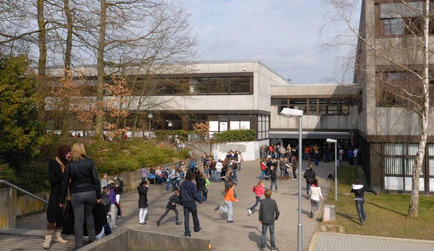 eine Treppe, die nach unten auf einen Hof führt, in dem sich viele Kinder bewegen; im Hintergrund ein großes Gebäude