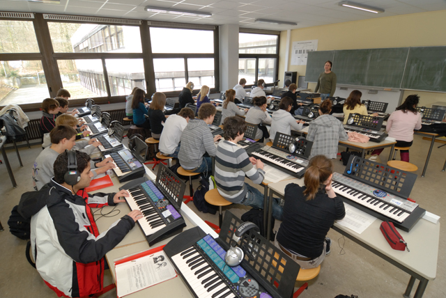 einen Klassenraum mit Tischreihen, an denen Jugendliche - teilweise mit Kopfhörern - vor Keyboards sitzen