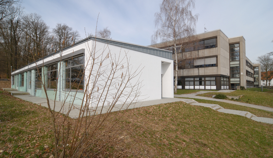 den Blick über eine Wiese mit einer weiß gestrichenen Halle mit großen Fenstern