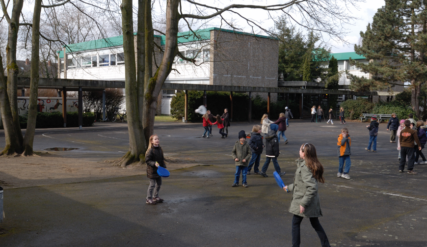 Kinder, die auf einem großen Schulhof zwischen einigen Bäumen spielen