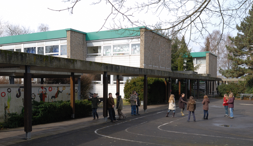 einen Hof, in dem sich einige Kinder befinden, dahinter ein überdachter Weg zu einem Gebäude