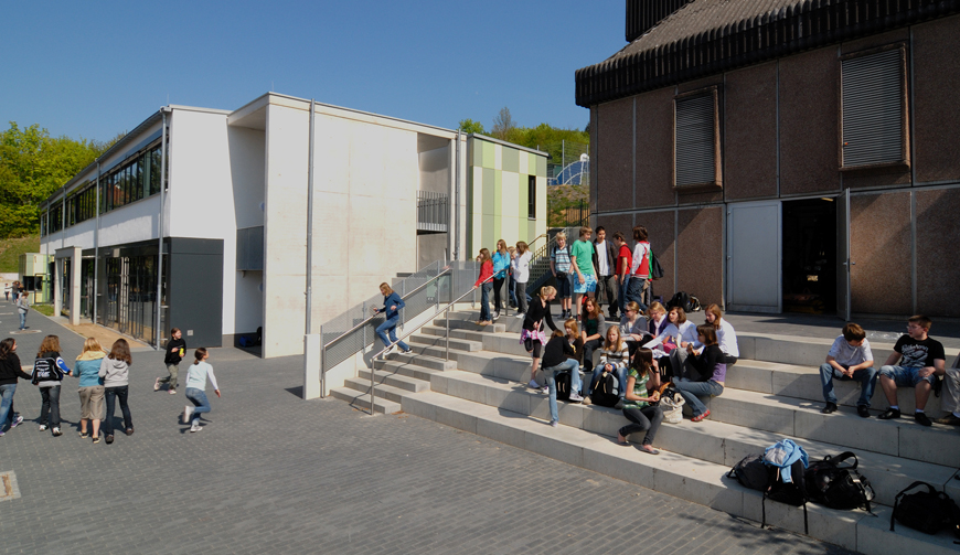 den Blick über einen Hof und Treppen, auf denen Schüler sitzen; im Hintergrund Gebäude