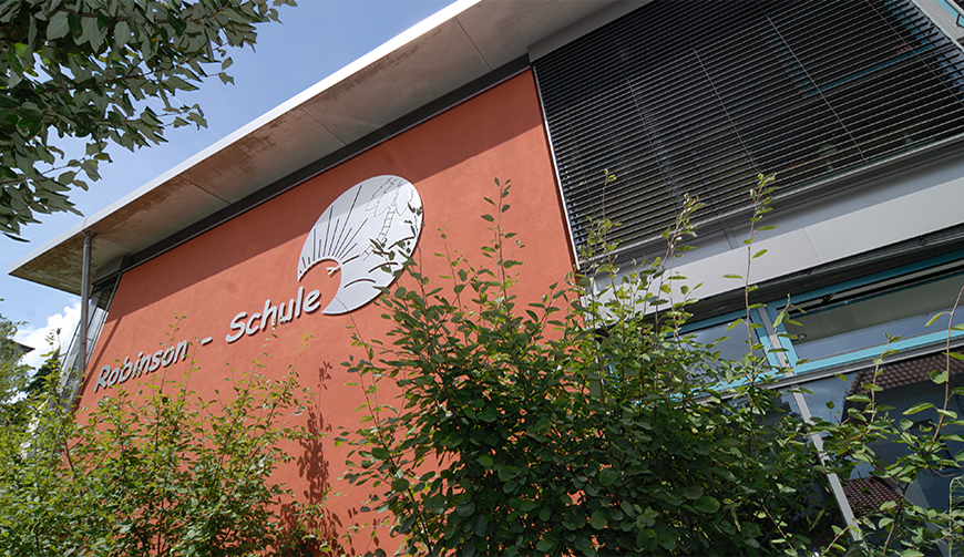 den Ausschnitt eines rot gestrichenen Gebäudes mit dem Schriftzug Robinson-Schule