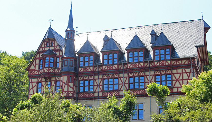 ein von Bäumen und Büschen gesäumtes Fachwerk-Gebäude mit vielen Giebeln