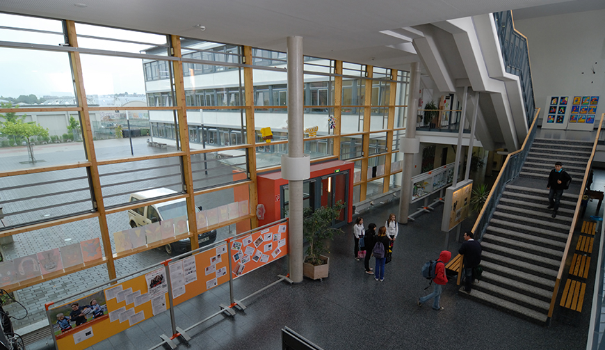 Blick von oben in eine große Eingangshalle mit Glasfront und einem Treppenhaus, in der bunte Ausstellungstafeln stehen