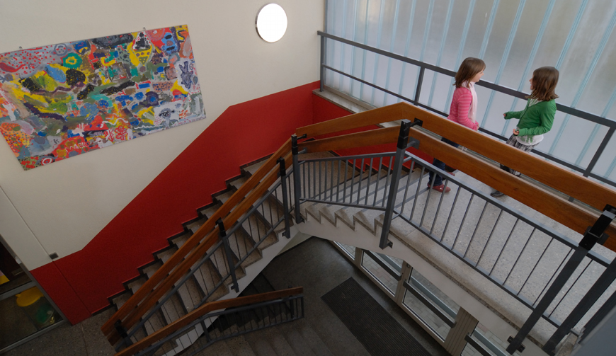 den Blick von oben in ein großes Treppenhaus, in dem ein buntes Bild an der Wand hängt