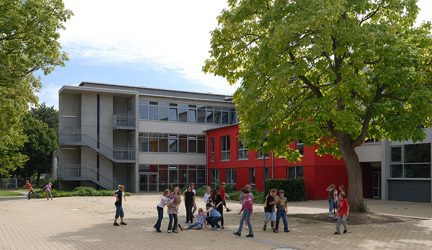 einen Hof, in dem einige Schüler stehen, mit einem rot-grauen Gebäude im Hintergrund
