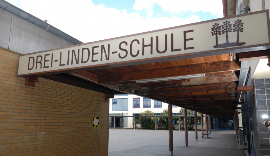 Blick auf einen Hof und einen überdachten Gang, an dessen vorderem Ende Drei-Linden-Schule steht