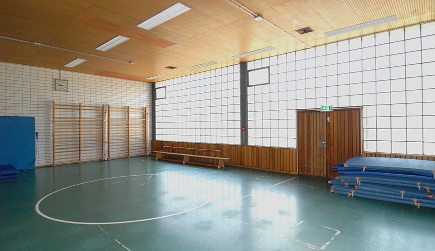 den Blick in eine große, leere Sporthalle mit einigen Turnmatten und Kletterwänden