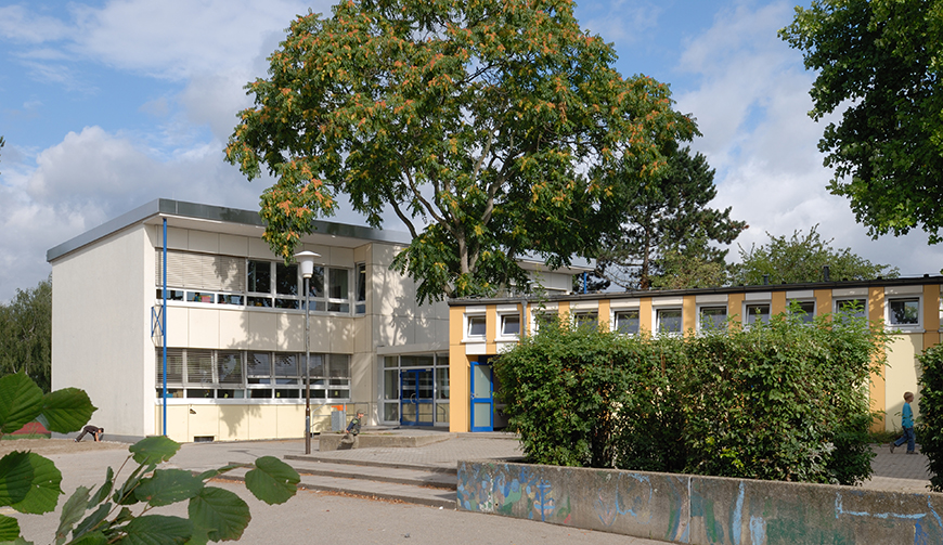 den Blick auf zwei Gebäude, im Vordergrund ein großer Hof mit Hecken