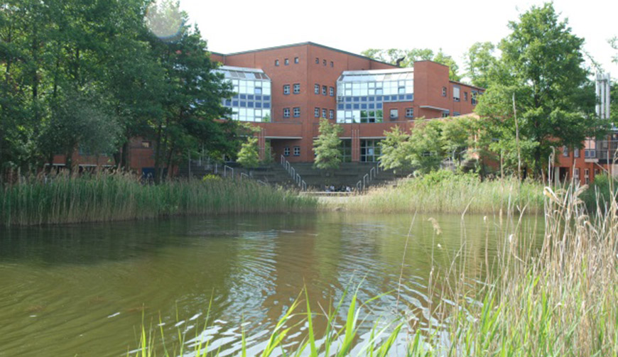 den Blick über einen großen Teich auf einige Bäume und ein großes Gebäude im Hintergrund