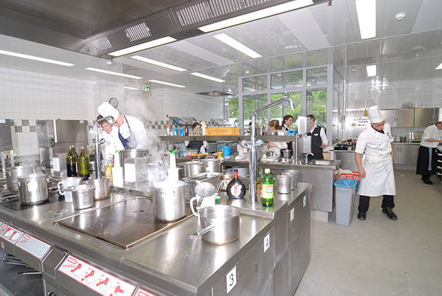eine Restaurantküche mit Edelstahl-Ausstattung, in der einige Köche arbeiten