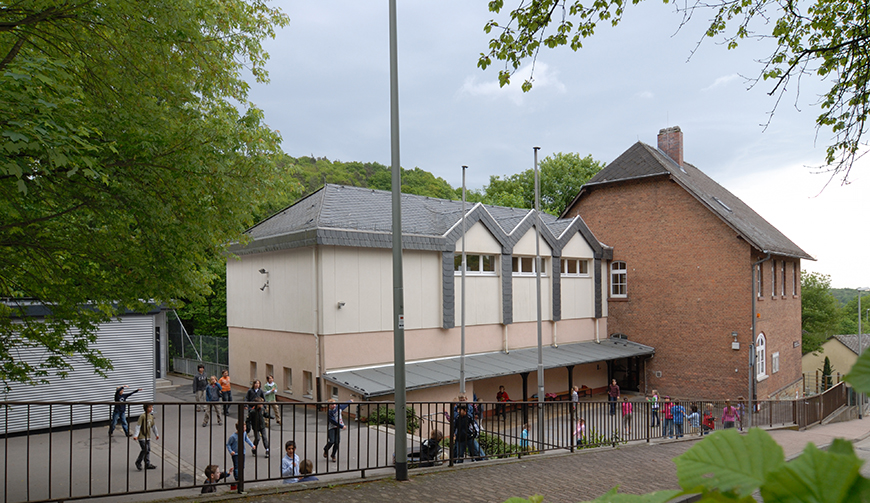 den Blick von einem Hügel über einen Zaun in einen Hof, in dem Kinder spielen, mit Gebäuden im Hintergrund