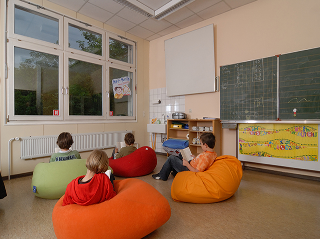 vier Kinder, die in einem Raum mit Tafel auf bunten Sitzsäcken sitzen und lesen