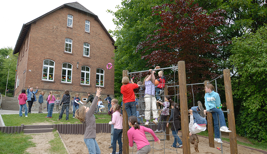 ein Klettergerüst voller Kinder, dahinter eine Wiese mit spielenden Kindern und ein großes Haus