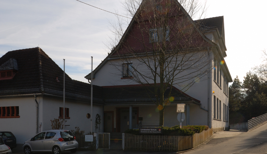 den Ausschnitt einer Straße; im Vordergrund steht ein kahler Baum, dahinter einige Häuser