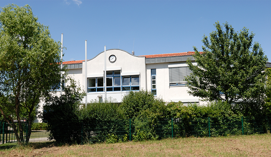 den Blick über eine Wiese und Hecken auf ein großes weißes Gebäude