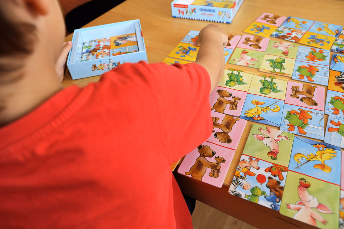 Ein Kind legt bunte Tierkarten eines Domino-Spiels auf einem Tisch aus