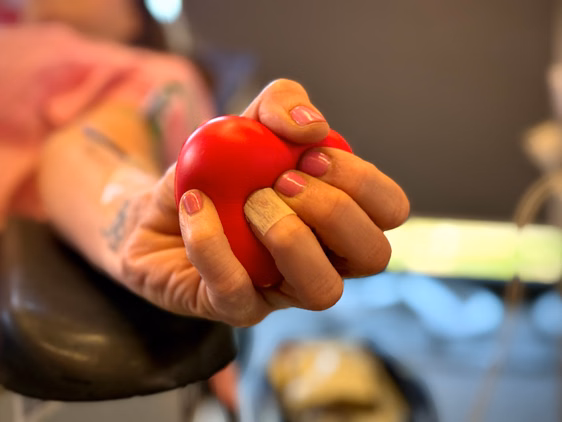 Eine Frau bei der Blutspende, die einen roten Ball in Herzoptik in der Hand hält