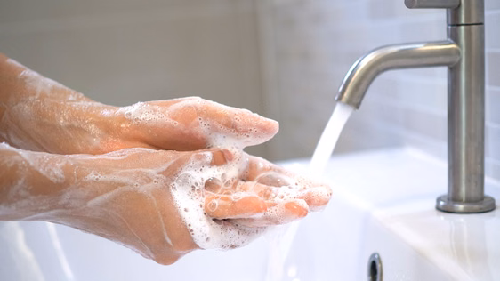 Eingeseifte Hände, die unter einen laufenden Wasserhahn gehalten werden